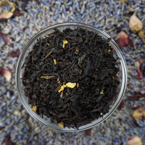 Schwarzteeblätter mit gelb-orangefarbenen Fruchtstücken und Blütenblättern