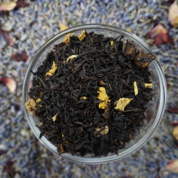 Schwarzteeblätter mit gelb-orangefarbenen Fruchtstücken und Blütenblättern