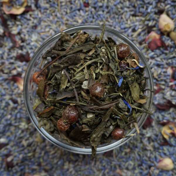 Grün- und Weißteeblätter mit roten Beeren, blauen Blüten und orangefarbenen Fruchtstücken
